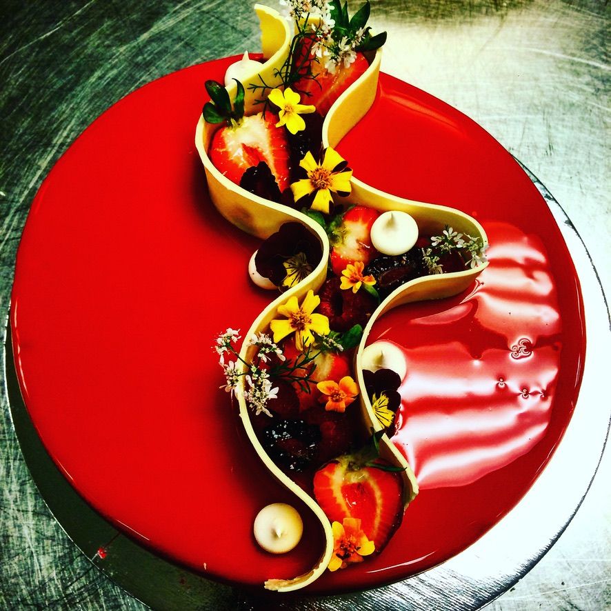 Entremets au glaçage rouge, ruban de chocolat blanc, fruits et fleurs